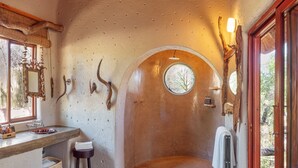 A rustic bathroom with a stone wall, a round window, a wooden bench, and a sink with bottles.