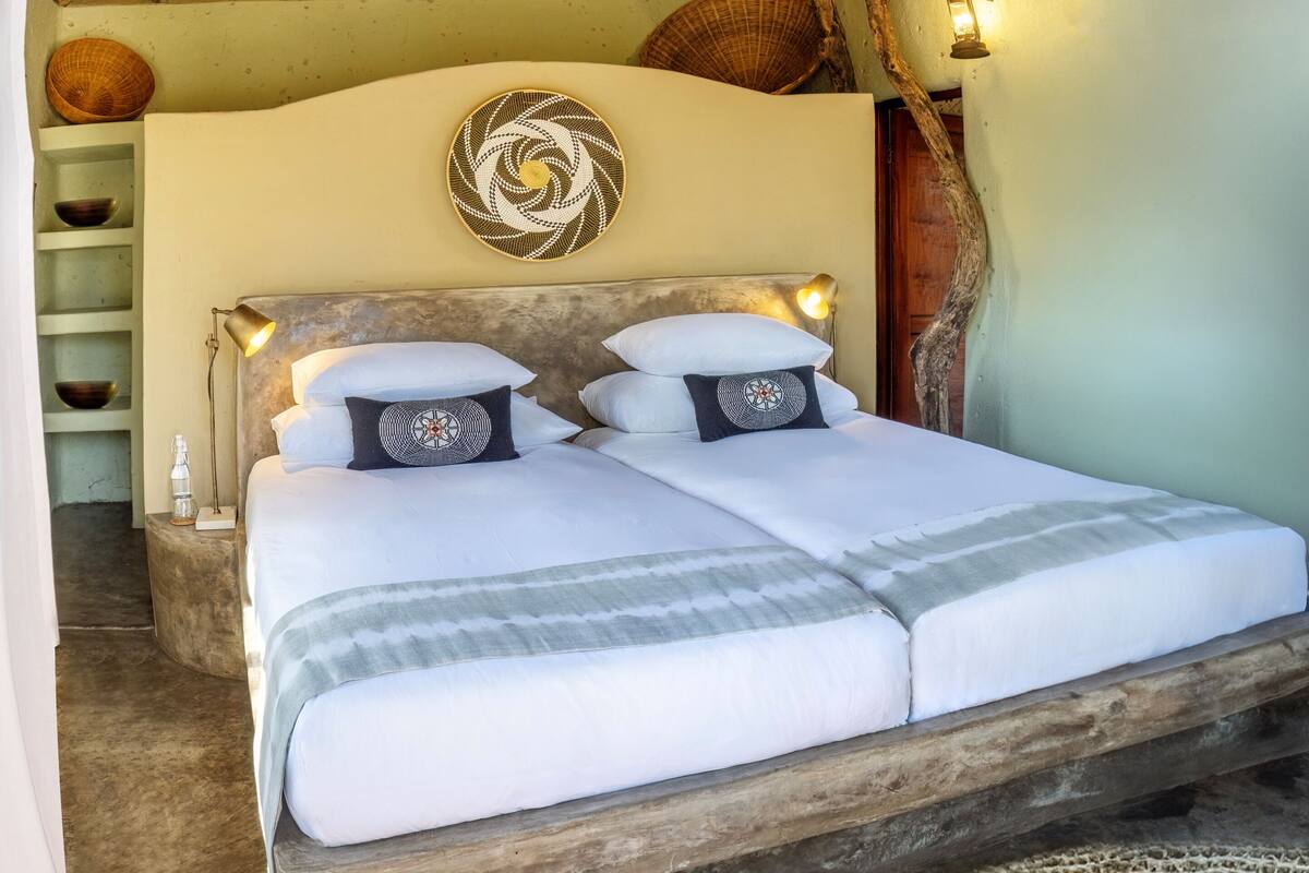 A double bed with white linens and two decorative pillows, a wooden headboard, and a wall-mounted decorative plate.