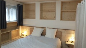 Quarto com cabeceira de madeira, duas mesas de cabeceira com luminárias, cama com roupa de cama branca e uma janela com cortinas.