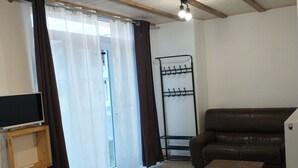 Sala de estar com sofá de couro marrom, mesa de centro de madeira, TV sobre suporte de madeira, varal de metal e porta de vidro deslizante com cortinas.