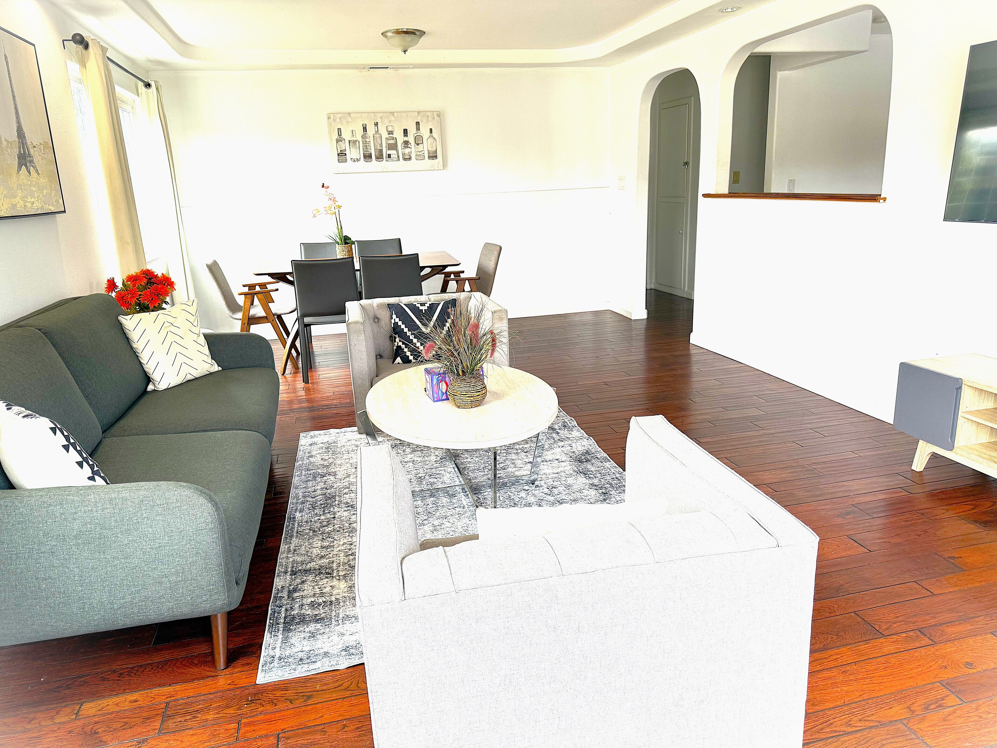 A living room with a grey sofa, a coffee table with a vase, and a dining area with chairs and a table.