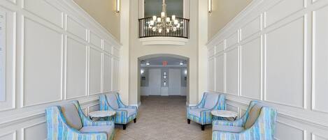 A lobby with a high ceiling, a chandelier, and two sets of blue patterned chairs with small tables.
