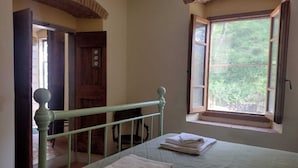 A bedroom with a bed, a window with a view of greenery, a wooden door, and a metal railing. - Apartment in Farmhouse (Pelago)