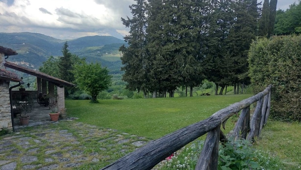 A rustic stone building with a patio, surrounded by a grassy field and trees, overlooking a valley. - Apartment in Farmhouse (Pelago)