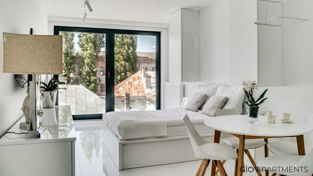 A modern bedroom with a bed, bedside table, lamp, and a view of the outside. - Luxury Apt • AC • Workspace • 5 min to Downtown (Kraków)