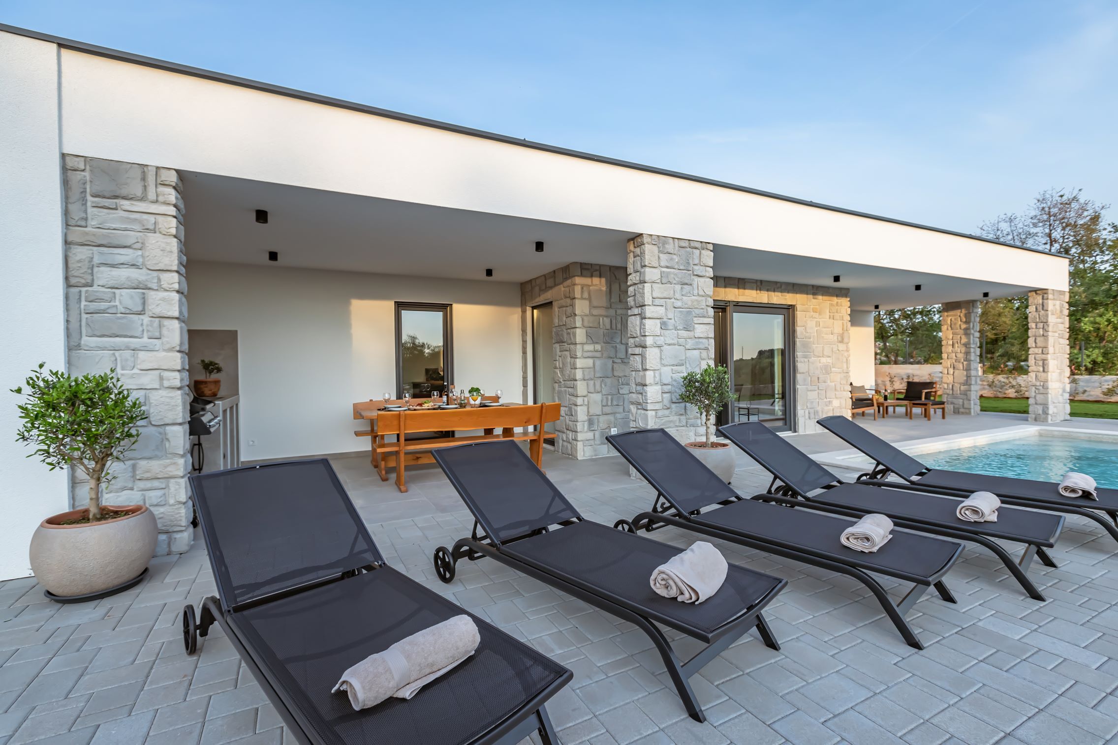 A modern outdoor pool area with lounge chairs and a dining table.