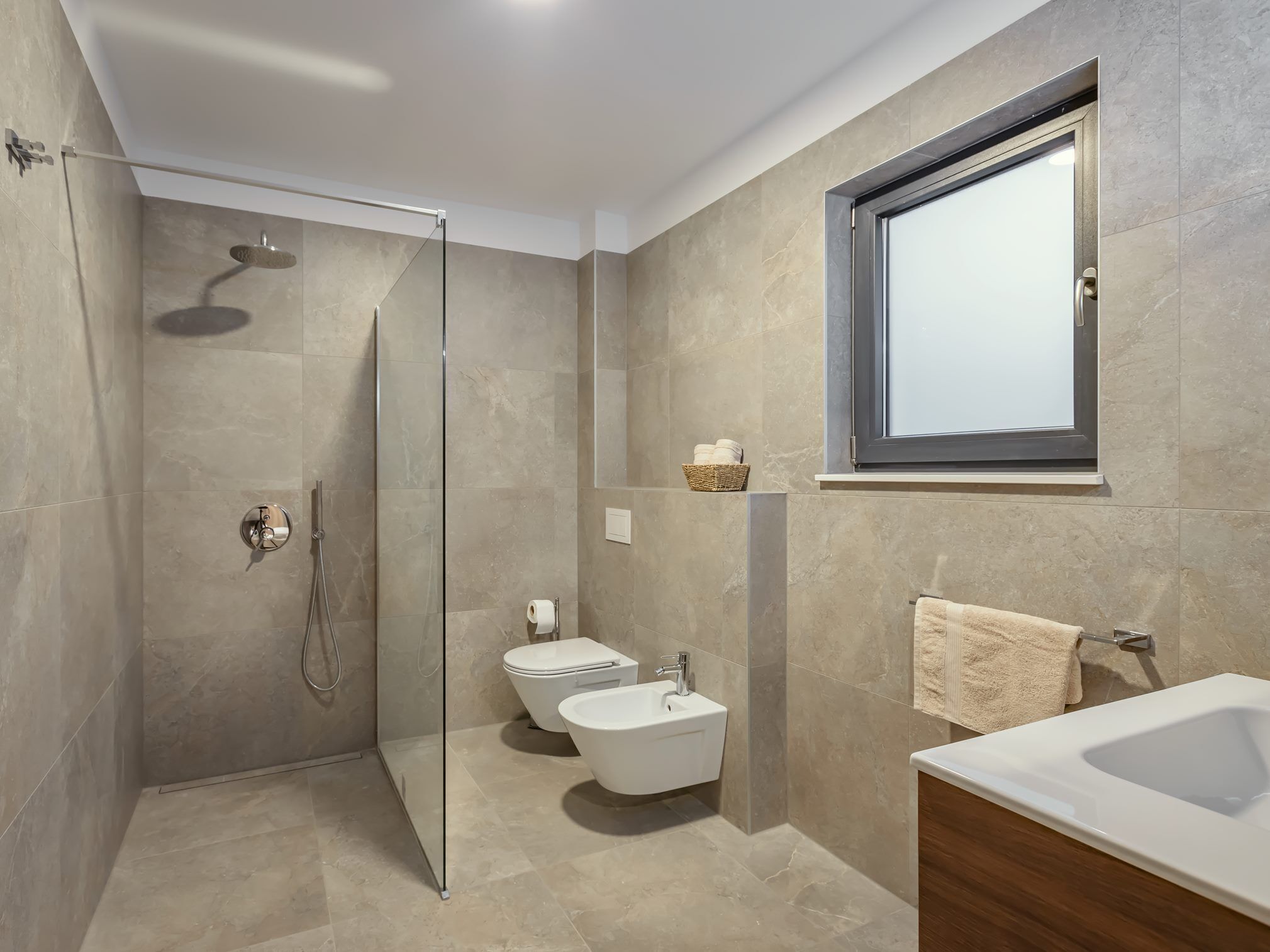 A modern bathroom with a glass-enclosed shower, a toilet, a bidet, and a sink.