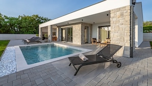 Une maison moderne dotée d’une piscine, de murs en pierre et d’un patio avec des chaises longues.