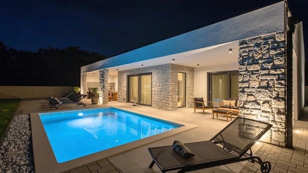 Une maison moderne dotée d’une piscine, de murs en pierre et d’un espace salon extérieur.
