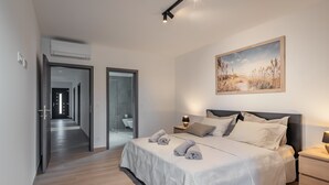Une chambre moderne avec un grand lit, une table de chevet avec une lampe, un tableau au mur et un couloir menant à une autre pièce.