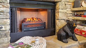 A fireplace with a stone wall, a bear statue, and a magazine on a cushion. - Spacious 4BR Pigeon Forge Cabin with Hot Tub, Game Room, and Mountain Views (Pigeon Forge)
