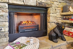 A fireplace with a stone wall, a bear statue, and a magazine on a cushion.