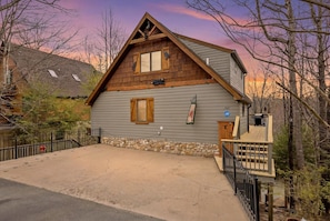 A two-story log cabin with a stone foundation, a wooden deck, and a stone wall.