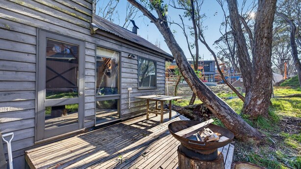 A wooden cabin with a deck, a fire pit, and a view of the surrounding trees and landscape. - Coho Chalet - Dinner Plain (Dinner Plain)