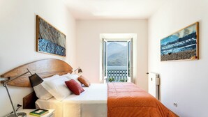 Un dormitorio con cama, lámpara de noche y vistas a las montañas desde la puerta del balcón.