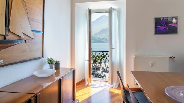 Un interior moderno con una mesa de comedor de madera, una encimera de cocina, un balcón con vistas a las montañas y una obra de arte enmarcada en la pared.