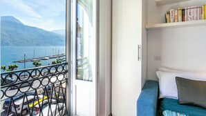 Un balcón con vistas a un lago y montañas, una puerta blanca y una estantería llena de libros.