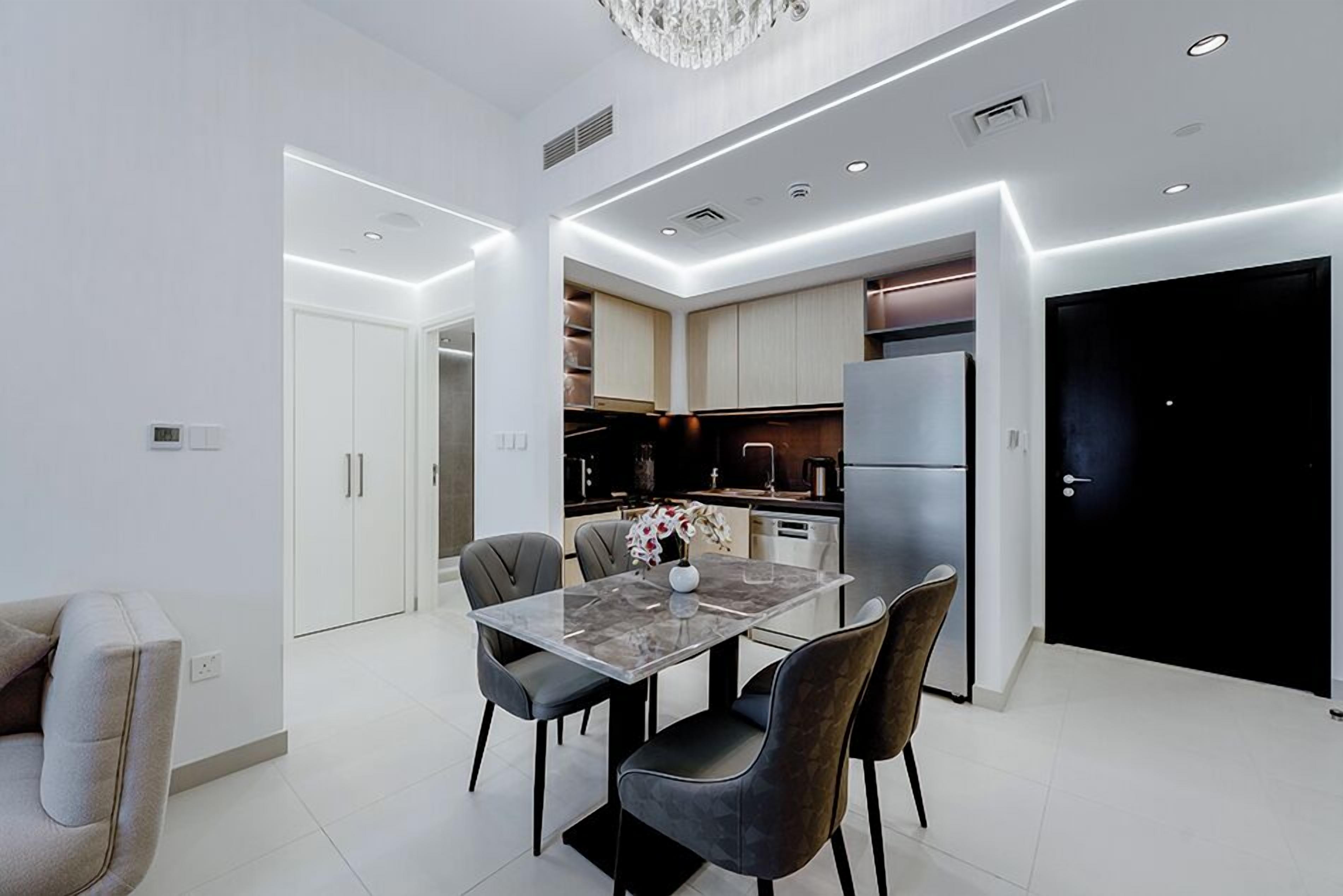 A modern kitchen with a dining area, featuring a marble table, dark chairs, and a chandelier.
