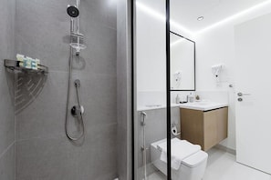 A modern bathroom with a glass-enclosed shower, a white toilet, and a vanity with a mirror. - Stayis- 1 BR Spacious & Luxury Apartment (Dubai)