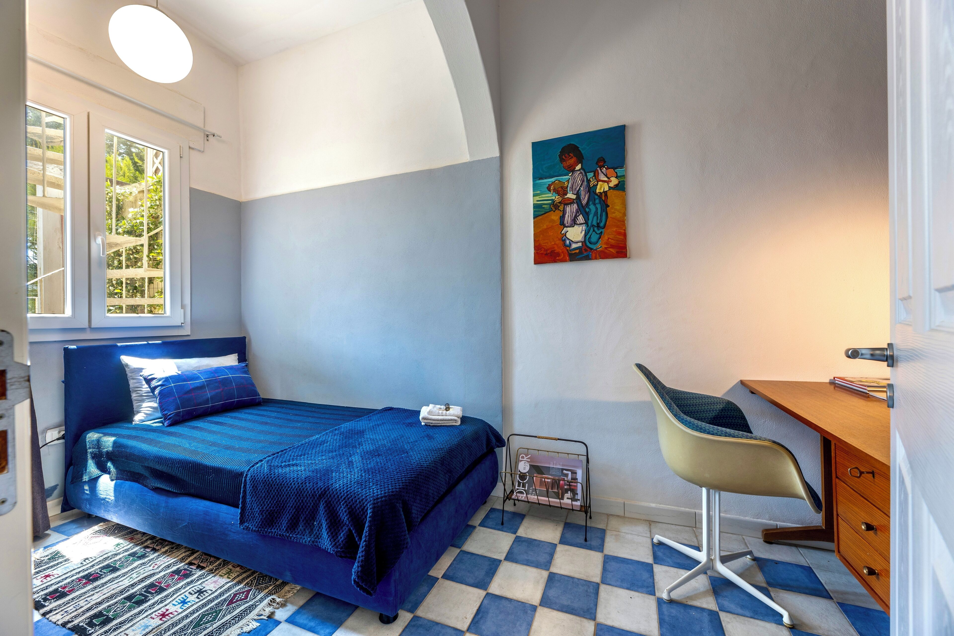 Ein Schlafzimmer mit einem Bett, einem Schreibtisch, einem Stuhl, einem Gemälde und einem Fenster.