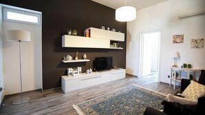 A modern living room with a flat-screen TV, white entertainment unit, and decorative items on shelves. - Le Terrazze sui Tetti di Noto by Wonderful Italy (Noto)