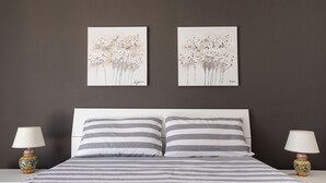 A bedroom with a bed, two bedside tables, two lamps, and two wall-mounted paintings. - Le Terrazze sui Tetti di Noto by Wonderful Italy (Noto)