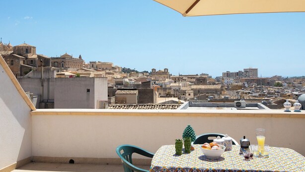 A balcony with a table set for breakfast, overlooking a cityscape with historic buildings. - Le Terrazze sui Tetti di Noto by Wonderful Italy (Noto)