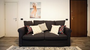 A dark-colored sofa with patterned cushions, a framed artwork above it, and a wooden door to the right. - Le Terrazze sui Tetti di Noto by Wonderful Italy (Noto)