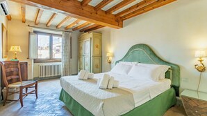A bedroom with a large bed, wooden beams, a window, a chair, and a radiator.