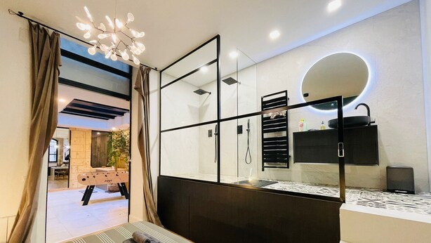 A modern bathroom with a large mirror, a shower, and a sink. There is a bed with towels on it. - Loft Bordelais (Bordeaux)