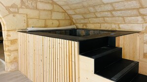 A spa area with a stone wall backdrop, a wooden bench, and a black heated floor. - Loft Bordelais (Bordeaux)