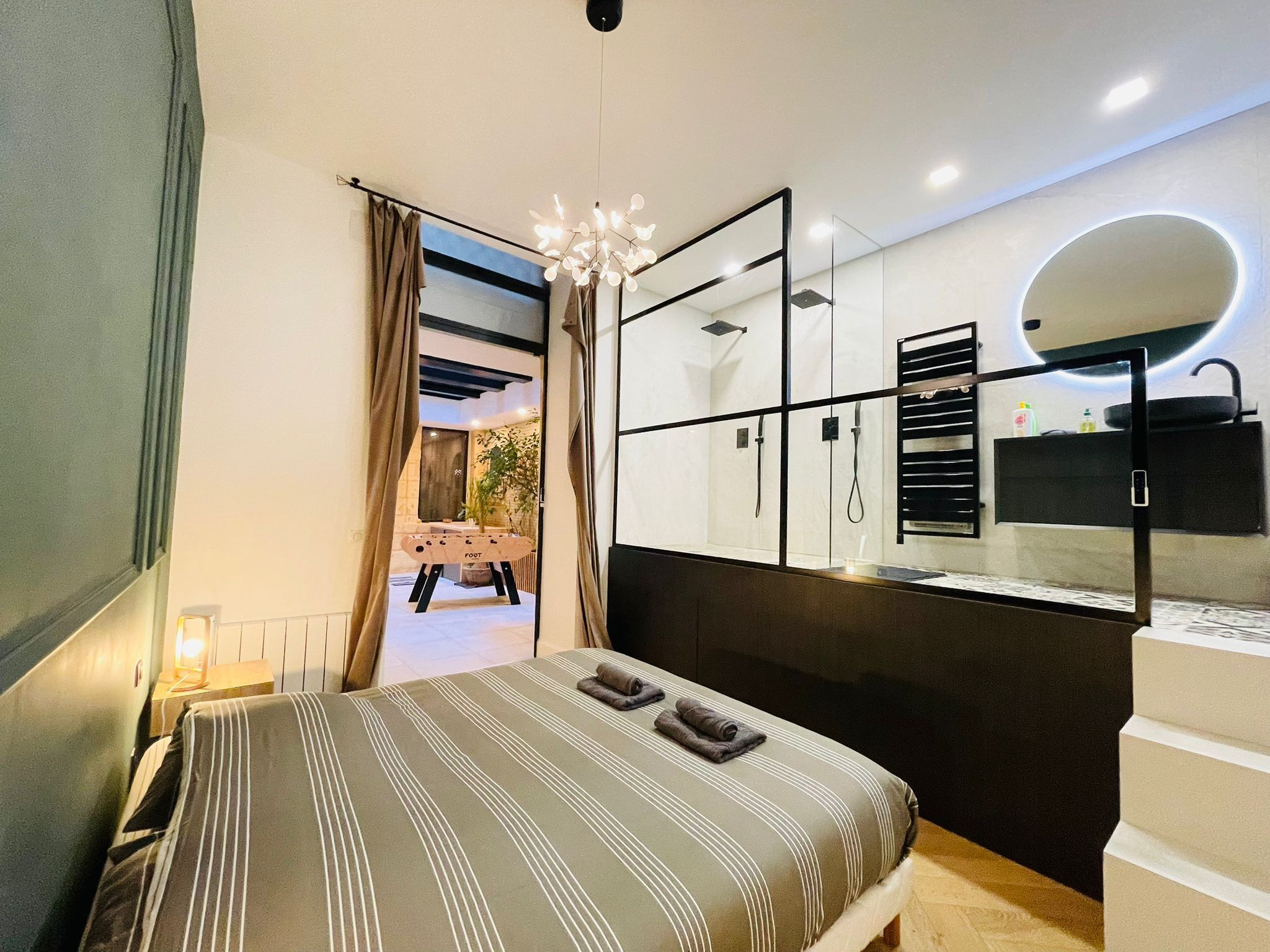 A modern bedroom with a bed, a shower area, and a vanity with a mirror.