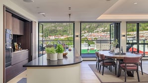 Eine moderne Küche mit dunklen Holzausziehtüren, einer schwarzen Arbeitsplatte und Blick auf eine Stadt durch große Fenster.