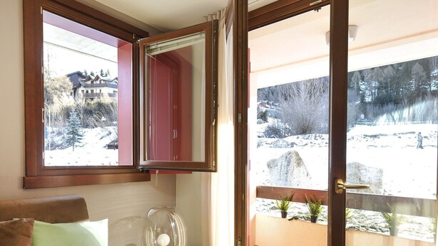 Ein Zimmer mit einer Couch, einem gläsernen Tisch, einem roten Schrank und einem Balkon mit Blick auf eine verschneite Landschaft.