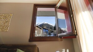 Ein Zimmer mit Fensterblick auf einen verschneiten Berg, ein fenster mit Holzrahmen und ein an der Wand befestigtes dekoratives Element.