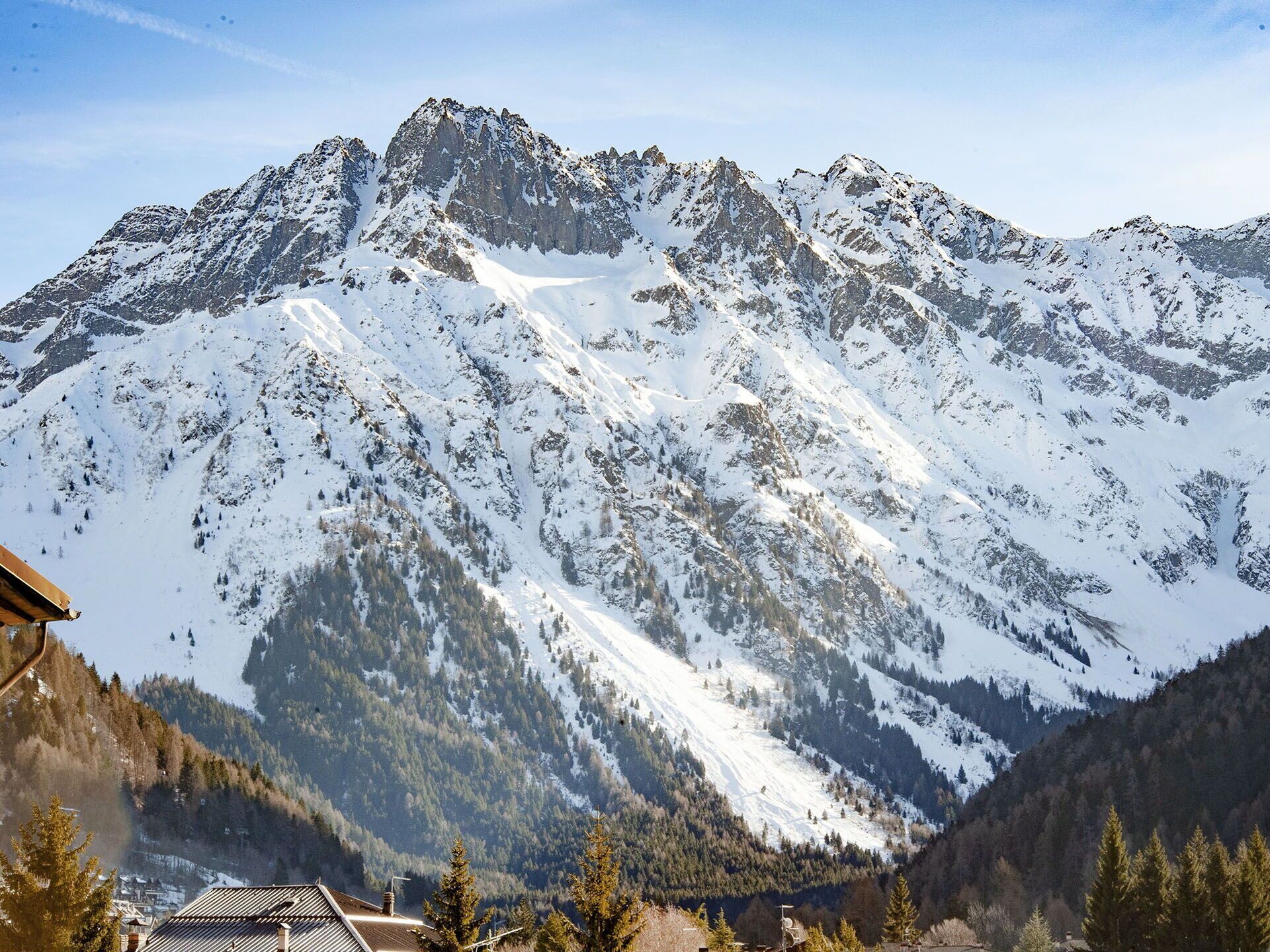 Una montaña con picos nevados y un valle con edificios y árboles.