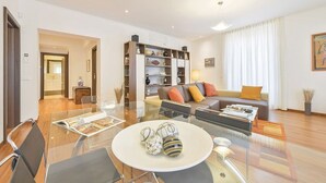 A modern living room with a glass dining table, a sofa, and a bookshelf. - Anselmi Modern 2 Br Flat By Halldis (Florence)