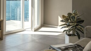 A room with a large sliding glass door leading to a balcony with a view of a lake and mountains. There is a framed picture on the wall, a potted plant, and a hat on the floor. - d'Ocalée Holiday Experience (Omegna)