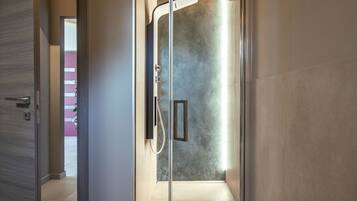 Un baño moderno con ducha, un banco de madera con toalla y rosas, y vista a un edificio rosa en el exterior.