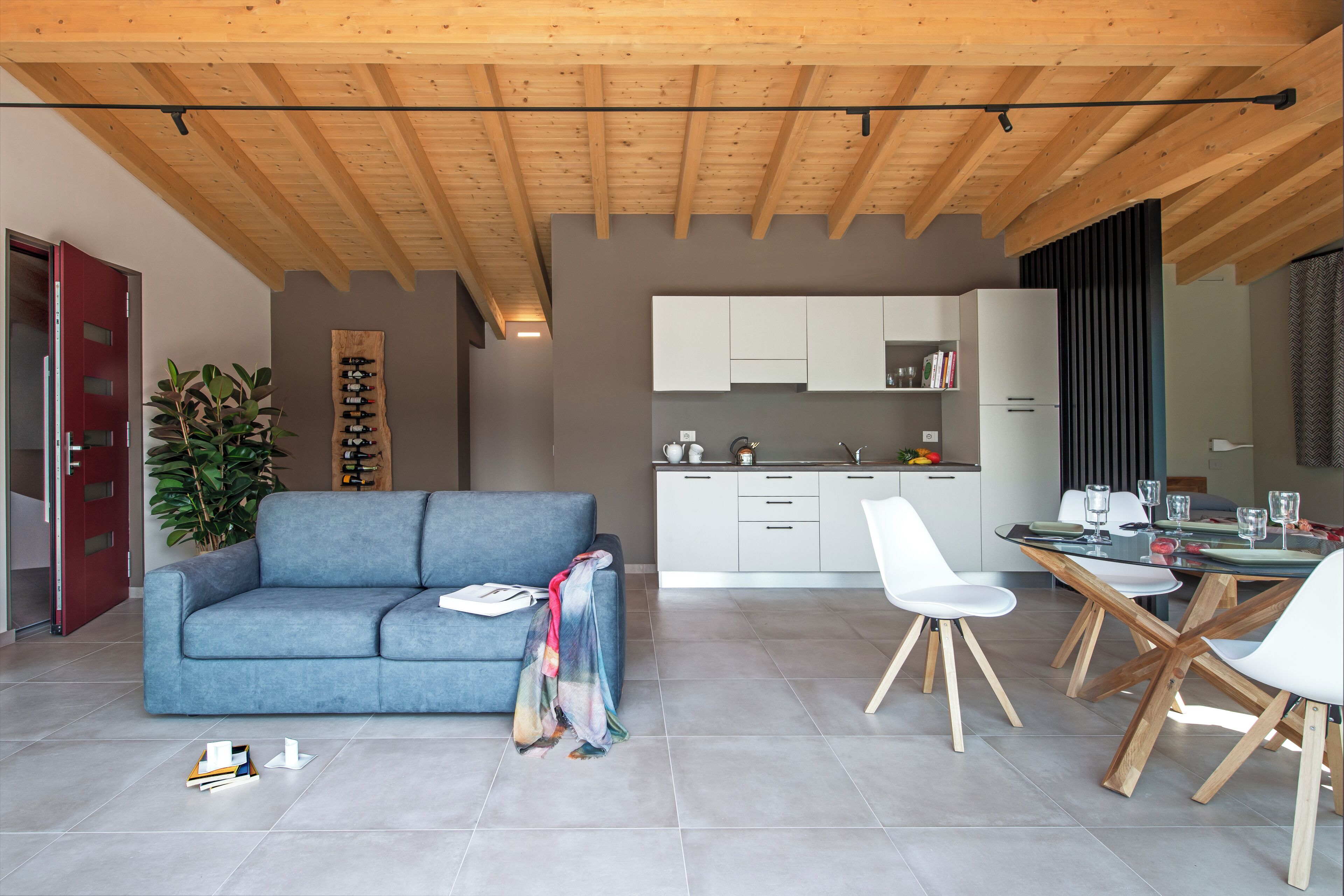 Een moderne woonkamer met een blauwe bank, een eettafel met stoelen, een keuken met witte kasten en een rode deur.