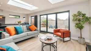 A modern living room with a grey sofa, orange and blue cushions, a wooden coffee table, and a potted plant. - Family Seaside Escape - Near Viking Bay (Broadstairs)