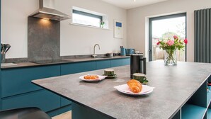 A modern kitchen with teal cabinetry, a large island, and a window with a view. - Family Seaside Escape - Near Viking Bay (Broadstairs)