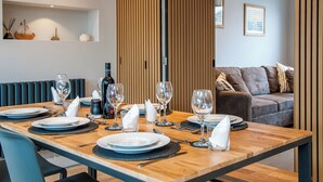 A dining area with a wooden table set for four, including plates, glasses, and cutlery. There is a brown sofa in the background and a vertical wooden panel dividing the space. - Family Seaside Escape - Near Viking Bay (Broadstairs)