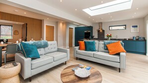 A modern living room with two grey sofas, a coffee table, and a kitchen area in the background. - Family Seaside Escape - Near Viking Bay (Broadstairs)