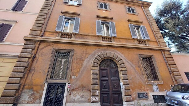 A building with a central arched entrance, multiple windows with shutters, and a car parked in front. - Studio con Soppalco • Via Gregoriana • Vicino Piazza di Spagna (Rome)