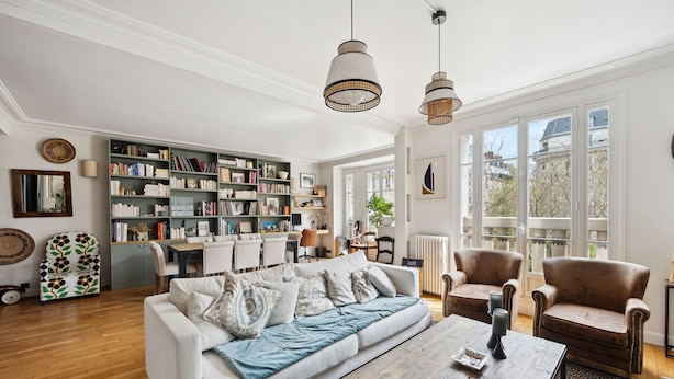 A spacious living room with a white sofa, two leather armchairs, a coffee table, and a large bookshelf filled with books. - Industry Chic, by Veeve (Paris)