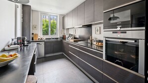A modern kitchen with dark cabinetry, stainless steel appliances, and a large window providing natural light. - Industry Chic, by Veeve (Paris)