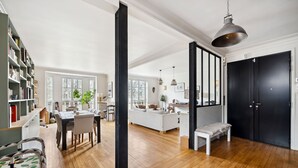 A spacious living area with a dining table, chairs, a sofa, and a bench. There is a bookshelf, a hanging light fixture, and a black door. - Industry Chic, by Veeve (Paris)