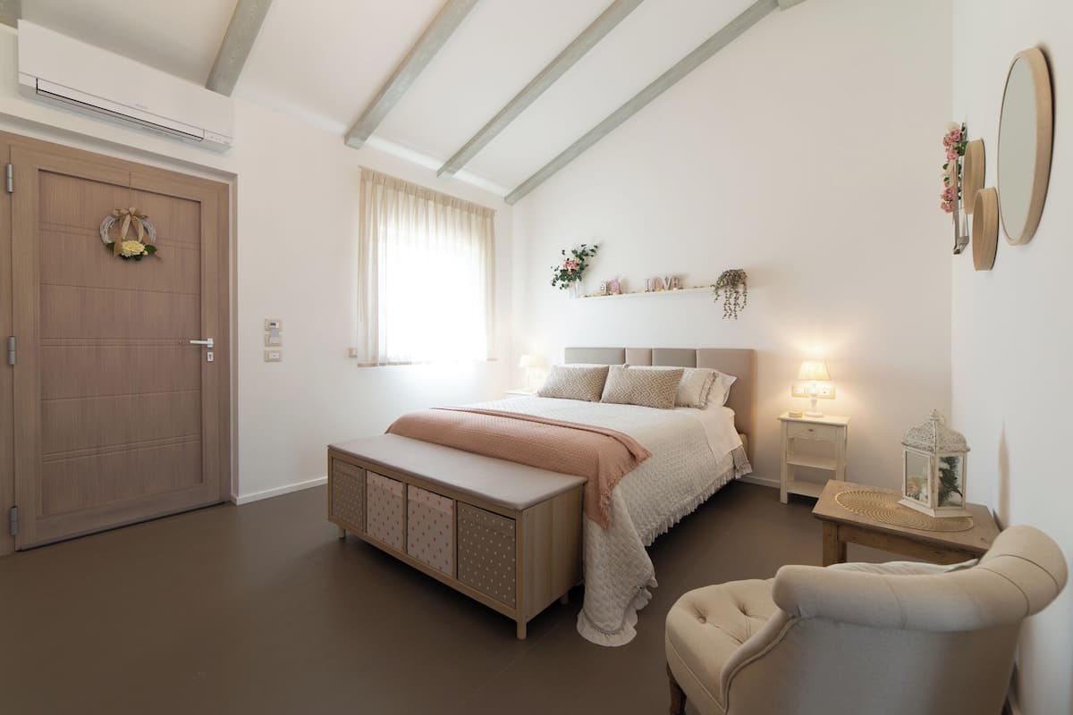 Quarto com cama grande, mesas de cabeceira, uma cadeira, guarda-roupa e janela com cortinas.