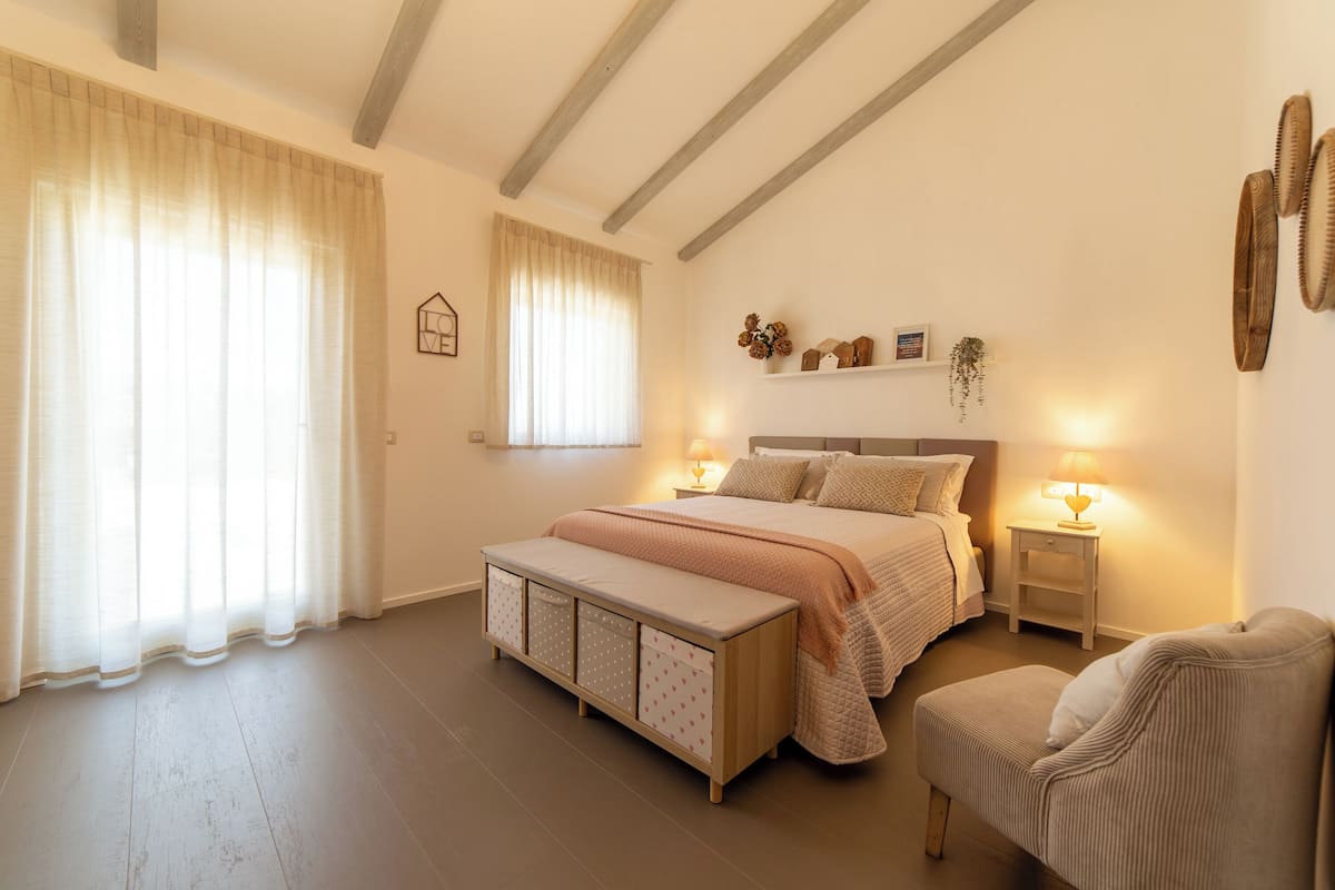 Quarto com cama, mesas de cabeceira, um banco e uma cadeira.